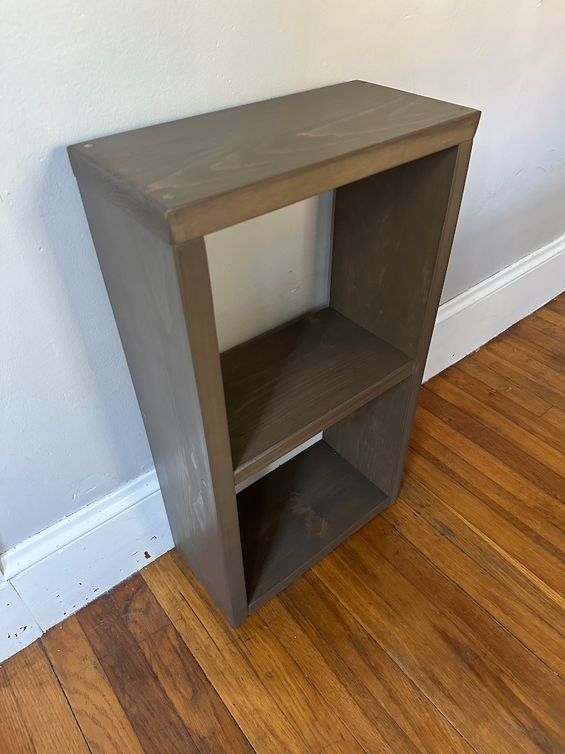 May include: A two-shelf wooden bookcase with a dark brown stain finish. The bookcase is made of solid wood and has a simple, modern design.