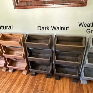 May include: Three wooden shelf units with three shelves each. The shelves are in three different finishes: natural, dark walnut, and weathered gray.