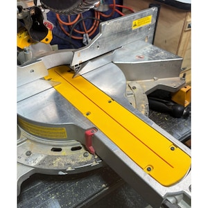 Może przedstawiać: Srebrno-żółta piła ukośna z żółtą osłoną ostrza. Piła ma srebrne ostrze i żółtą podstawę. Piła jest przeznaczona do cięcia drewna i innych materiałów. Jest to elektronarzędzie.