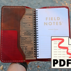 以下が含まれることがあります： 赤い革のノートカバーで、前面に茶色の革のポケットが付いています。ノートが開いていて、白いページに「FIELD NOTES」と「56-Week Planner」の文字が見えます。