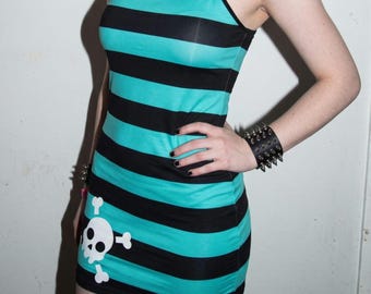 Puede incluir: Un vestido corto sin mangas con rayas horizontales negras y de color verde azulado. En la parte inferior izquierda del vestido hay un estampado gráfico blanco de una calavera con tibias cruzadas. Tiene tirantes finos.