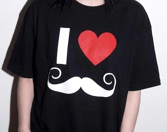 May include: A black short-sleeved t-shirt featuring a graphic print on the front. The design consists of a white letter I, a solid red heart, and a large white handlebar mustache positioned below the heart, creating an I love mustache motif.