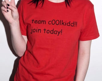 May include: A bright red short-sleeved t-shirt featuring black text printed on the chest that reads team c00lkidd!! join today! The garment has a classic crew neckline and a standard fit, providing a simple and bold visual appearance.