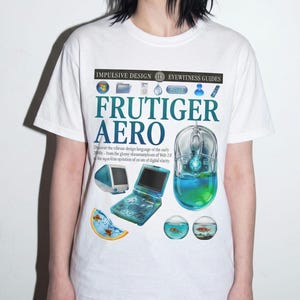 Puede incluir: Una camiseta blanca con un estampado gráfico que incluye el texto "IMPULSIVE DESIGN EYEWITNESS GUIDES" y "FRUTIGER AERO". El diseño muestra varios iconos digitales de principios de los 2000, un monitor de ordenador y una consola portátil.