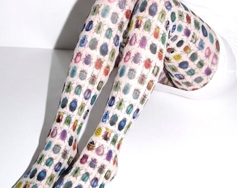May include: Sheer white tights featuring an all-over repeating pattern of colorful beetles in various shades of red, blue, green, yellow, and purple. The hosiery covers the legs from the feet up to the upper thighs with a consistent insect print.