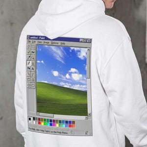 May include: A white hooded sweatshirt featuring a graphic print on the back of a computer software interface titled untitled - Paint. The graphic displays a toolbar, a color palette, and a landscape image of a green hill under a blue sky.