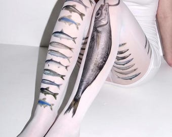 May include: White tights featuring a large, detailed graphic of a fish hanging from a hook on the right thigh, with a vertical row of smaller, varied fish illustrations running down the left leg and additional fish prints on the side.