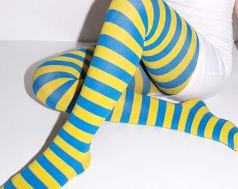 May include: Opaque tights featuring a vibrant horizontal striped pattern in alternating bright yellow and royal blue colors. The hosiery covers the legs completely, extending from the feet up to the upper thighs with a consistent striped design.