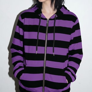 May include: A zip-up hoodie featuring horizontal black and purple stripes. The garment includes a hood with black drawstring cords, a full-length silver-toned metal zip down the centre, and two front pockets integrated into the striped pattern.
