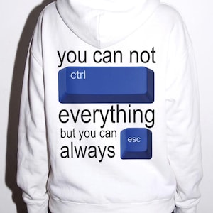 May include: A white hooded sweatshirt featuring black text that reads you can not followed by a blue ctrl keyboard key graphic, then the word everything, followed by but you can always and a blue esc keyboard key graphic.