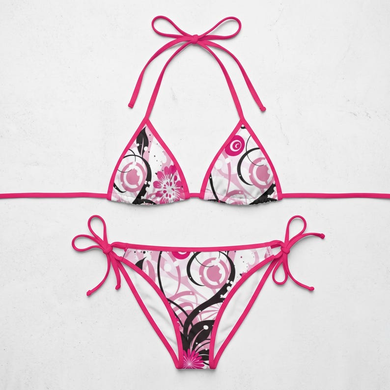 K&ouml;nnte beinhalten: Ein zweiteiliger Bikini mit wei&szlig;em Hintergrund und einem abstrakten Blumen- und Wirbelmuster in leuchtendem Pink und Schwarz. Das Oberteil hat Triangel-Cups mit pinkfarbenen B&auml;ndern, das Unterteil verf&uuml;gt &uuml;ber seitliche Bindeb&auml;nder.