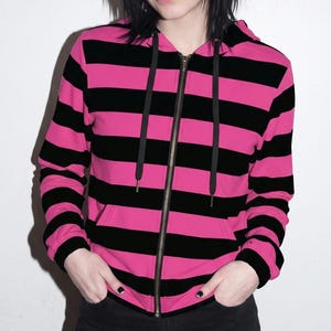 May include: A long-sleeve zip-up hoodie featuring horizontal stripes in alternating hot pink and black. The garment includes a hood with black drawstring cords, a full-length front zipper, and two front pockets at the waistline.