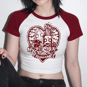 Op de afbeelding: Een wit kort raglan t-shirt met donkerrode mouwen en een donkerrode kraag. De voorkant heeft een donkerrode grafische print van twee gestileerde figuren in een hartvorm met de tekst My Chemical Romance onderaan gedrukt.