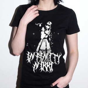 Puede incluir: Una camiseta negra de manga corta con un estampado gráfico blanco de un personaje estilo anime con vestido, rodeado de pequeñas estrellas y una pequeña criatura. Debajo del personaje, el texto Infinity Nikki está impreso en una fuente estilizada.