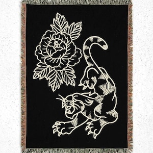 May include: A rectangular woven throw blanket with a black background featuring a large, cream-colored line art illustration of a tiger and a peony flower. The blanket has a fringed edge with multi-colored threads along the vertical sides.