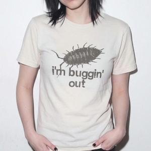 May include: A cream-coloured short-sleeve t-shirt featuring a dark brown graphic of an isopod insect centred on the chest. Below the insect illustration, the text reads "i'm buggin' out" in a dark brown, rounded, lowercase sans-serif font.
