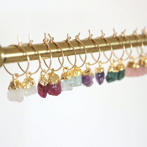 Peut inclure: Un ensemble de boucles d'oreilles créoles en or avec différentes pierres semi-précieuses qui pendent. Les pierres comprennent le blanc, le rose, le vert, le violet et le bleu.