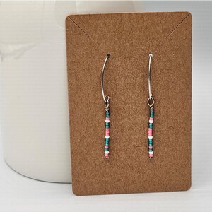 May include: A pair of dangle earrings with a silver wire and pink and teal beads.
