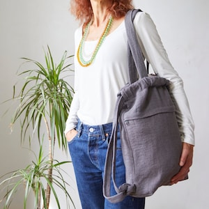 May include: A grey drawstring backpack with a zipped pocket and adjustable straps. The backpack is made from a soft, textured fabric.