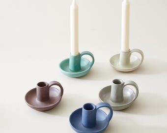May include: Five ceramic candle holders in different colors: mineral brown, sea glass green, ocean blue, seafoam beige, and cream sand. Each holder has a small handle and a wide base.
