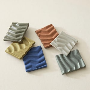 Puede incluir: Un conjunto de seis jaboneras rectangulares con una superficie ondulada y estriada. Las piezas presentan acabados en colores mate que incluyen verde oliva, amarillo mostaza, azul intenso, terracota, gris claro y verde salvia.