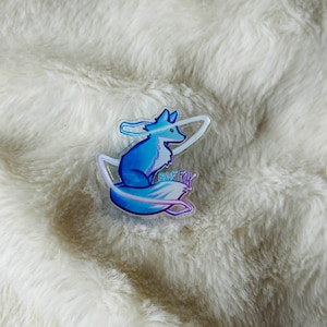 Peut inclure: Un renard bleu avec une queue violette assis dans un cercle clair et iridescent. Le cercle a un contour blanc et le texte "BLUE FOX" est écrit en blanc à l'intérieur du cercle.