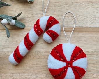 Puede incluir: Dos adornos navideños de fieltro, una caña de azúcar y una menta, ambos decorados con lentejuelas rojas.