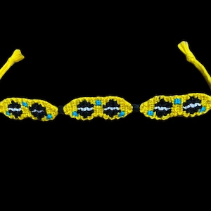 Puede incluir: Un brazalete de amistad amarillo con patrones geométricos negros y azules.