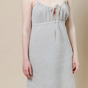May include: A light gray linen slip dress with a lace trim and a tie at the neckline.