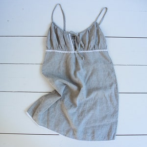 May include: A gray linen nightgown with white lace trim. The straps are thin and adjustable. The gown is loose fitting and has a gathered neckline.