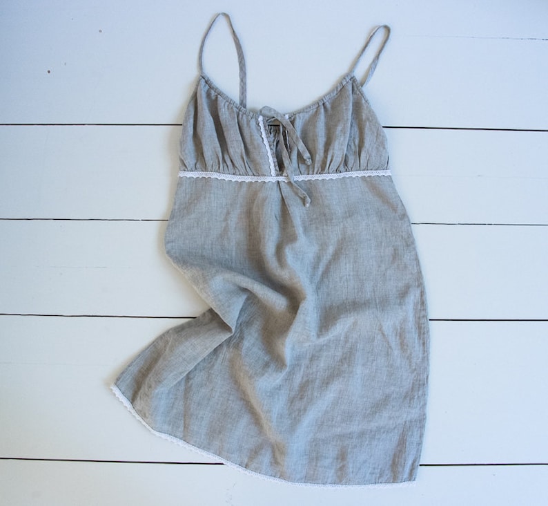 May include: A gray linen nightgown with white lace trim. The straps are thin and adjustable. The gown is loose fitting and has a gathered neckline.