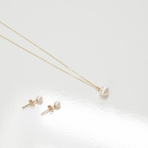 May include: A gold chain necklace featuring a single round white pearl pendant and a pair of matching gold stud earrings, each set with a small round white pearl. The jewelry set is displayed against a plain, light-colored surface.