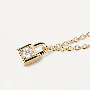 May include: A gold-colored padlock pendant necklace with a small, clear gemstone set in the center. The pendant is square-shaped with rounded edges. The chain is also gold-colored and has a delicate link design. The background is plain white.