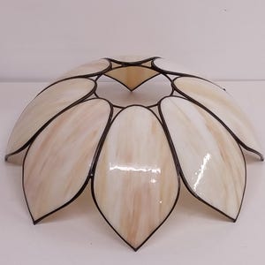 May include: A stained glass lampshade in a floral design. The shade features petal-shaped panels in cream and light brown hues, outlined with dark metal. The design is reminiscent of a flower, with a central point and radiating petals.