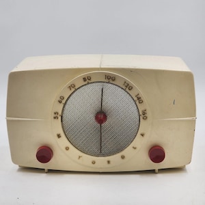 Peut inclure: Radio Motorola vintage, dans un boîtier crème avec des boutons rouges. Le cadran circulaire affiche des chiffres et un cache-haut-parleur en maille. Le mot "Motorola" est imprimé sur le devant. Un classique de l'électronique du milieu du siècle.