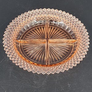 Puede incluir: Un plato de servir vintage de cristal rosa dividido en cuatro secciones. El plato presenta una zona circular central con un diseño de rayos de sol, rodeada por un borde con diseño de diamantes.