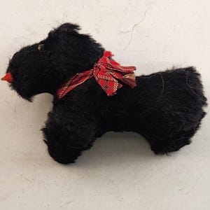 May include: A black plush dog figurine with a red and gold plaid ribbon around its neck. The dog has a red nose and a fluffy, textured appearance. The figurine is a decorative item.