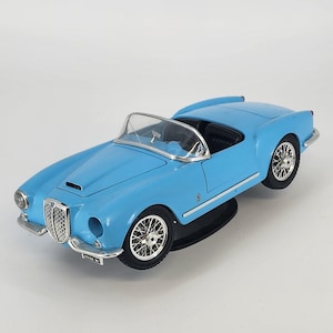 May include: A light blue vintage toy car with a silver windshield and chrome accents. The classic convertible has black tires and detailed silver wire wheels. The car's front features a chrome grill and a license plate.