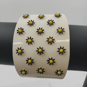 Brazalete vintage de plástico con forro dorado y delicado diseño floral en negro y amarillo.
