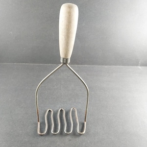 May include: A silver potato masher with a wooden handle. The masher has four wavy prongs.