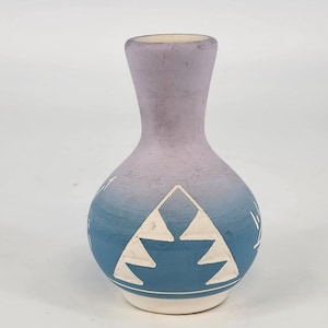 May include: A small decorative vase with a rounded body and a slender neck. The vase has a colour gradient from light purple to blue, with white geometric designs. The base is white.