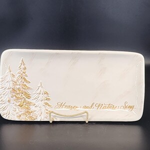 May include: Rectangular off-white serving tray with gold embossed pine trees and the text "Heaven and Nature Sing". The tray is supported by a gold metal stand. The tray has a lightly textured surface.
