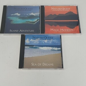 以下が含まれることがあります： 透明なプラスチックケースに入ったNatureQuestの音楽CD3枚。左上のカバーは青い海に囲まれた島で「Island Adventure」と題されています。右上のカバーは夕暮れの山々で「Magic Moments」と題されています。下のカバーは砂浜で「Sea of Dreams」と書かれています。
