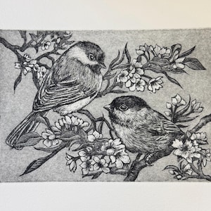 May include: A monochrome etching depicting two small birds on a flowering branch. The birds have dark heads and light bodies. The delicate flowers add detail to the artwork. The background is a light grey.