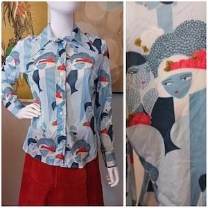 May include: Light blue button-down shirt with a repeating pattern of stylized faces wearing hats and holding flowers. The shirt has long sleeves and a pointed collar. The background has vertical stripes.