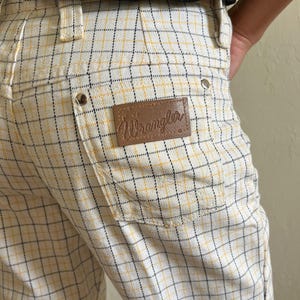 K&ouml;nnte beinhalten: Wei&szlig;e und gelbe karierte Hose mit einem braunen Leder-Wrangler-Etikett.
