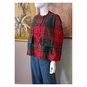 May include: A vintage red and green plaid jacket with three dark blue buttons. The jacket has a round collar and two small pockets. The jacket is displayed on a mannequin with blue jeans.