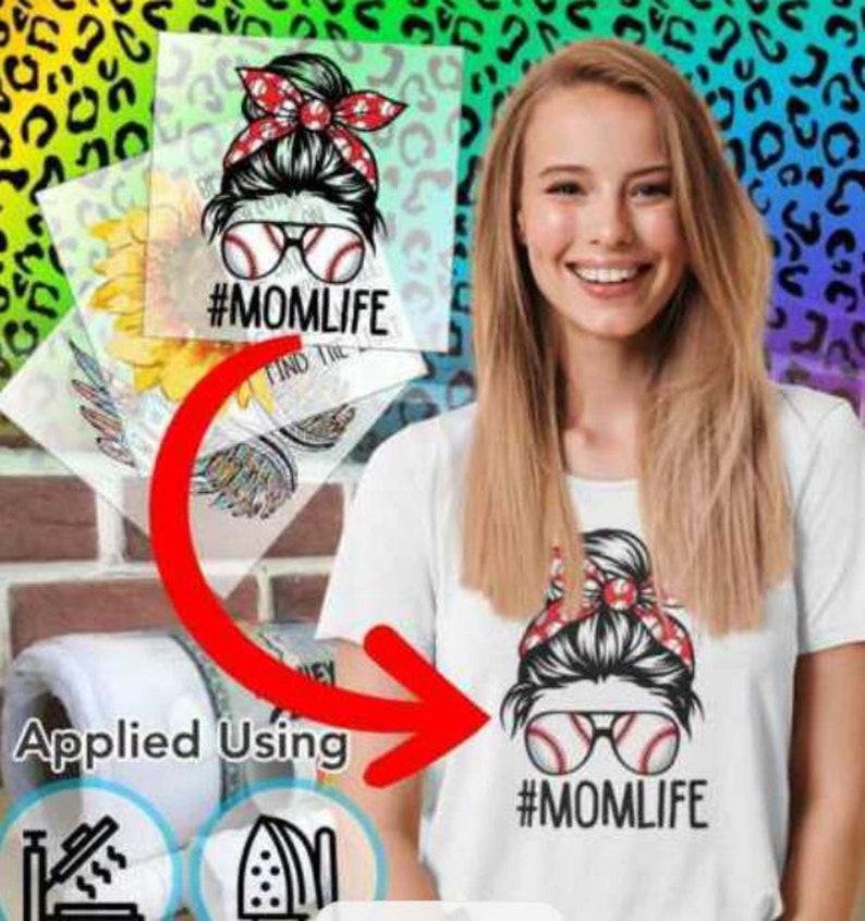May include: A white t-shirt with a black and white graphic of a woman with a messy bun, sunglasses, and a baseball. The text "#MOMLIFE" is below the graphic. The graphic is applied to the shirt using an iron.