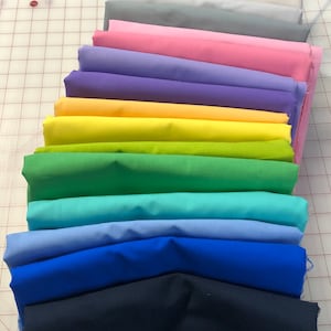 May include: A stack of 14 fabric swatches in various colours, including white, grey, pink, purple, yellow, green, blue, and navy. The fabric swatches are arranged in a rainbow pattern.