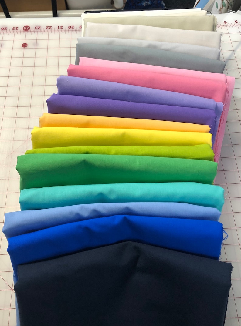 May include: A stack of 14 fabric swatches in various colours, including white, grey, pink, purple, yellow, green, blue, and navy. The fabric swatches are arranged in a rainbow pattern.